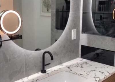 Modern bathroom vanity with marble countertop, round illuminated mirror, and black fixtures.